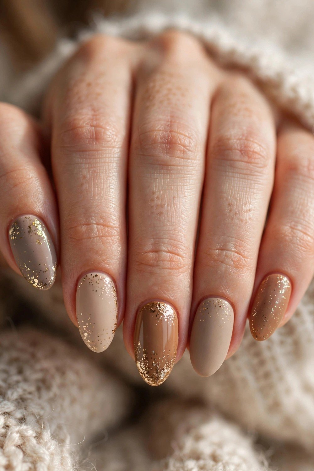 Close-up of nails in cozy latte beige, caramel and taupe tones with delicate gold glitter accents