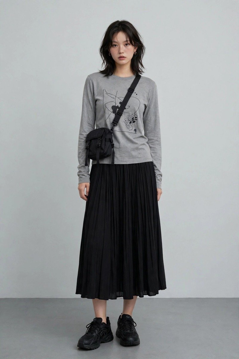 Grey graphic long-sleeve tee front-tucked into a black pleated midi skirt